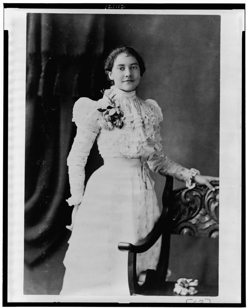 Young African American woman, three-quarter length portrait, standing, facing slightly right, with left hand on back of chair